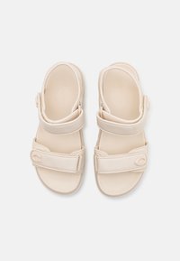 Beige sandaler med to justerbare stropper, teksturert fotseng og logodetalj på siden. Laget av glatt, holdbart materiale.