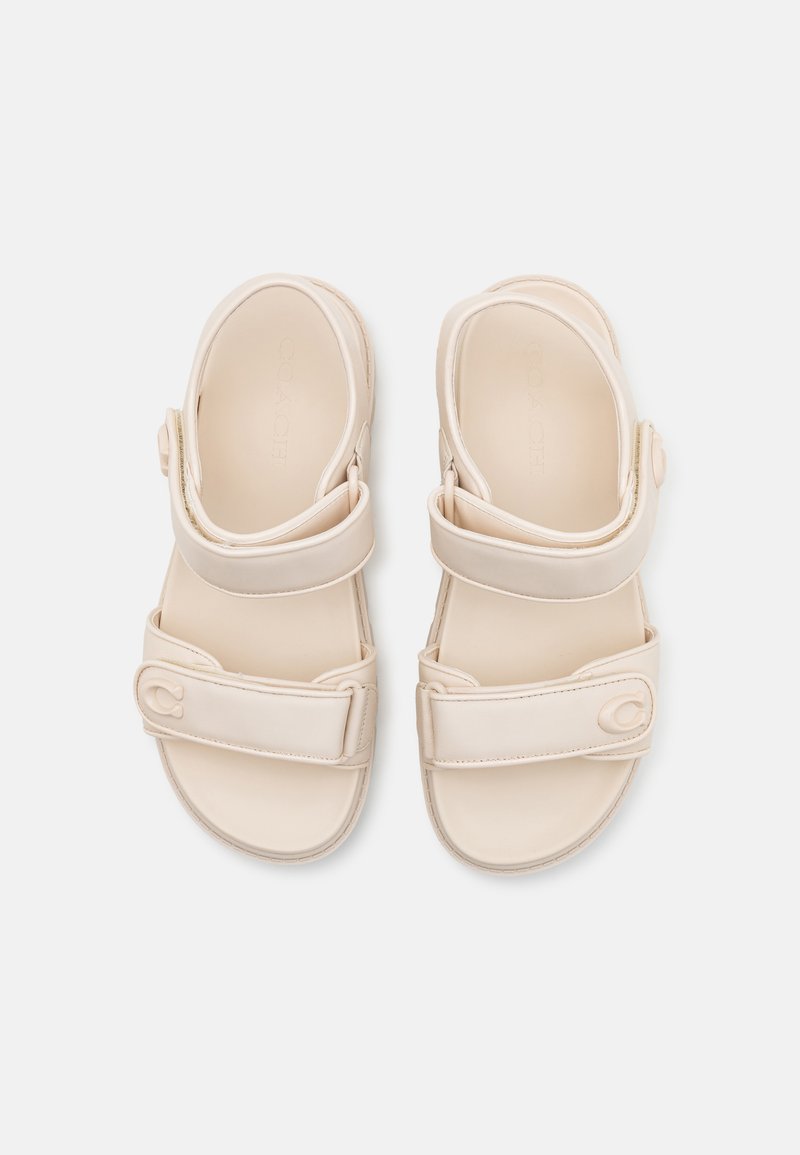 Beżowe sandały z dwiema regulowanymi paskami, teksturowaną wkładką i detalem logo po boku. Wykonane z gładkiego, trwałego materiału.