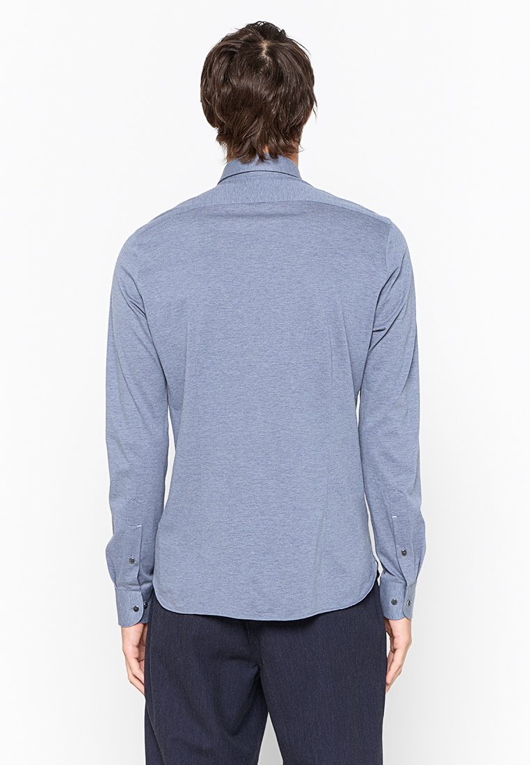 Camisa de manga larga en azul claro, hecha de una tela suave, con cuello puntiagudo y puños abotonados, con un dobladillo redondeado y parte trasera sin costuras.