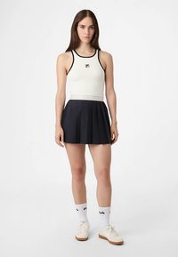 Valkoinen urheilullinen hihaton paita mustilla yksityiskohdilla yhdistettynä plissettyyn laivastonsiniseen hameeseen. Asun täydentävät valkoiset sukat ja kermaan vivahtavat lenkkarit.