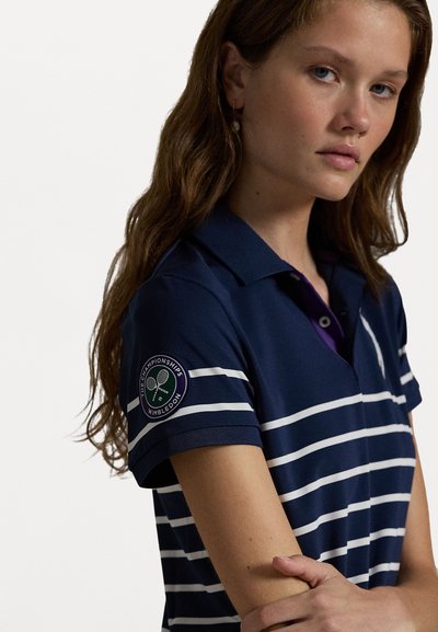 Marineblå stripete polo-skjorte i pustende stoff, med en lilla krage og et Wimbledon-logo merke på venstre erme. Komfortabel passform.