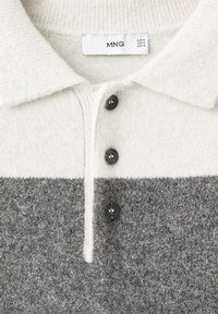 Suéter de punto con cuello, abotonado, con la mitad superior blanca y la mitad inferior gris, que presenta una etiqueta con información de tamaño en el interior del cuello.