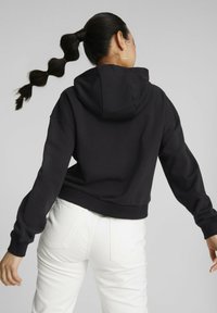 Sudadera negra recortada con un bolsillo frontal, mangas largas y capucha, combinada con jeans blancos texturizados. Tejido suave y corte holgado.