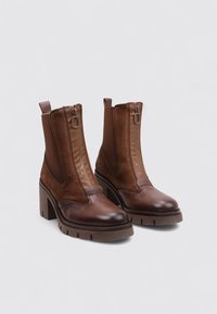 Botines marrones que combinan texturas lisas y de ante, con cierre de cremallera y tacón grueso con suela texturizada.