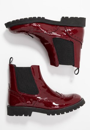 Paire de bottines Chelsea rouge foncé brillantes avec des panneaux latéraux élastiques noirs et des semelles épaisses à crampons noirs, vues de côté et de dessous.