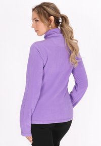 Lilla fleece-trøje med høj krave, lange ærmer og en glat overflade. Har en tætsiddende design og flade sømme for komfort.