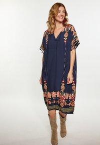 Laivansinis kaftan su ryškiais gėlėmis siuvinėjimais, su kutais ant rankovių ir laisva siluetu. Pora su šviesiais auliniais batais.