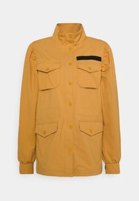 Gul jacka med hög krage, två bröstfickor och två sidofickor. Har puffärmar och en svart accent på fickan.