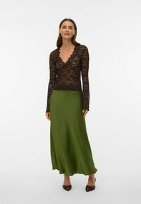 Czarna koronkowa bluzka z długimi rękawami i falowanym dekoltem w połączeniu z zieloną satynową maxi spódnicą o płynnej sylwetce i gładkiej fakturze.