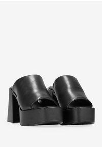 Sandalias de plataforma de cuero negro con la punta abierta, tiras anchas y un grueso tacón cuadrado. Textura suave y diseño minimalista.