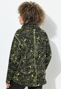 Sudadera de forro polar con cuello alto, que presenta un patrón abstracto en verde y amarillo, mangas largas y un ajuste relajado. Detalles visibles en las costuras.