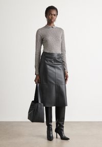 Gonna nera in pelle con taglio dritto, abbinata a una maglietta a maniche lunghe con fantasia. La modella tiene una borsa a mano nera, indossando stivali con tacco alto.