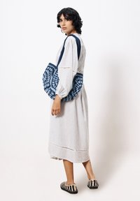 Blaue und weiße gemusterte Tragetasche mit einer Häkelstruktur, kombiniert mit einem hell gestreiften langen Kleid und schwarz-weißen gestreiften Hausschuhen.