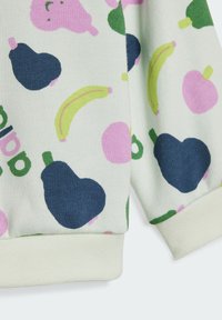 Suéter con una tela suave y ligera, adornado con un divertido patrón de frutas que incluye peras, plátanos y frutas rosas, sobre un fondo claro.