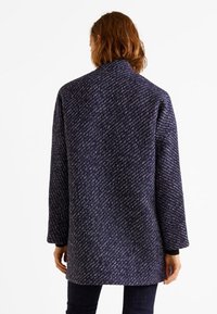 Marineblå tekstureret frakke med løs pasform, med høj krave, mønstret stof, synlige sømme og sænkede skuldre.