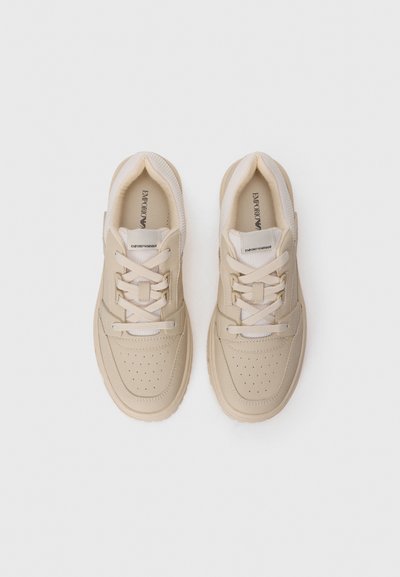 Par av beige Emporio Armani-sneakers med snören och perforerade tåhättor på en vit bakgrund, sedd ovanifrån.