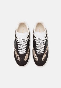 Baskets noires et beige clair avec un motif texturé effet peau de serpent, lacets blancs et un accent en cuir noir contrastant.