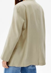 Beżowa lniana marynarka o luźnym kroju, z pojedynczym rozcięciem z tyłu i dwoma bocznymi kieszeniami. Posiada klapowy kołnierz i długie rękawy.