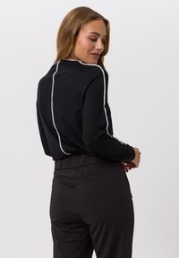 Black long-sleeve top with white piping along the spine and sleeves, made of soft material. Paired with black elastic waist pants.