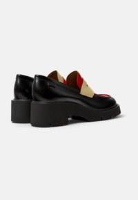 Scarpe in pelle nera con tacco largo nero, con un'accento beige e rosso sulla parte frontale. Texture liscia e design arrotondato.