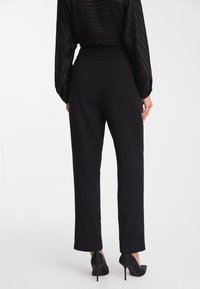 Czarne, dopasowane spodnie o prostym kroju i gładkiej teksturze. Noszone z przezroczystą, paskowaną czarną bluzką oraz wysokimi obcasami.