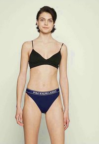 Mustmust bralette õhukeste rihmadega ja pehme tekstuuriga, koos tumesinise thongiga, millel on valge brändigraafika vööl. Lihtne, keha lähedal mudel.