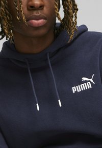 Sudadera con capucha azul marino hecha de suave forro polar, con bolsillo tipo canguro, logo de Puma en blanco y cordones ajustables con puntas de metal.
