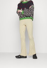 Strikket sweater med røde prikker, grønne accenter og et zigzag-mønster; cremefarvede flared bukser med tekstureret design; sorte sportssko.