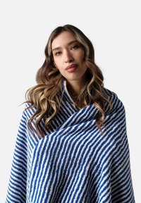 Chal azul y blanco a rayas con una tela suave y texturizada, drapeado de manera casual. Las rayas alternan entre patrones gruesos y delgados.