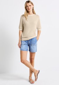 Kreemi neulottu villapusero lyhyillä hihoilla, yhdistettynä vaaleansinisiin denim-shorteihin. Asu on rento ja minimalistischinen.