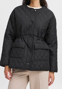 Sort quiltet jakke med rundet krave, trykknapper, to forlommer og en justerbar snor i taljen for pasform.