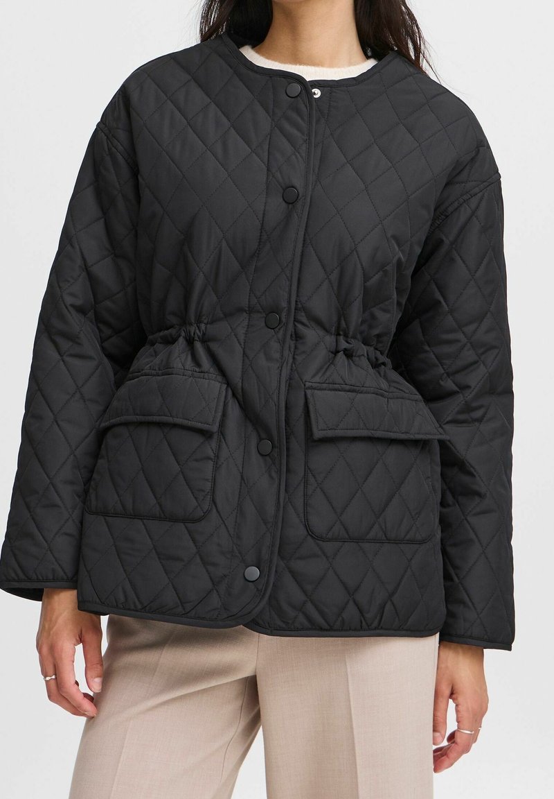 Sort quiltet jakke med rundet krave, trykknapper, to forlommer og en justerbar snor i taljen for pasform.