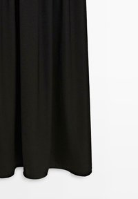 Czarna midi spódnica z delikatnymi plisami wisząca na białym tle, ukazująca fakturę tkaniny i gładki dół.