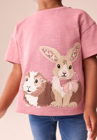 T-shirt rose à manches courtes avec broderies de lapin et de cochon d'Inde, ornées d'accents floraux sur les oreilles du lapin et un noeud.