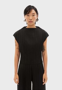 Zwarte, geribbelde jumpsuit met een hoge hals en korte mouwen. Het materiaal lijkt textuur te hebben, met verticale lijnen die door het ontwerp lopen.