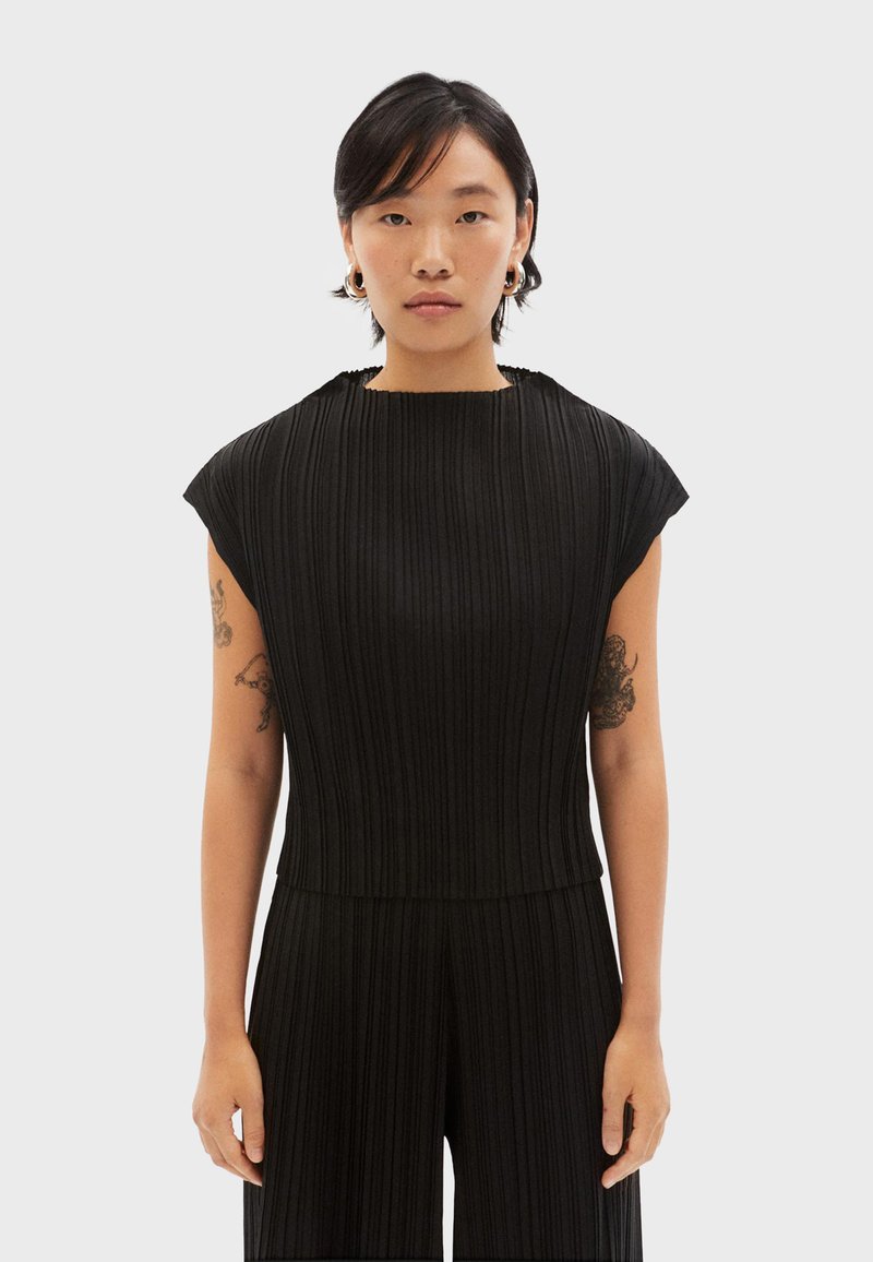 Zwarte, geribbelde jumpsuit met een hoge hals en korte mouwen. Het materiaal lijkt textuur te hebben, met verticale lijnen die door het ontwerp lopen.