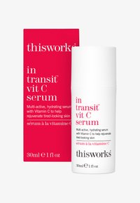 Thisworks in transit Vit C Serum, 30ml. Weißer zylindrischer Flakon mit pinkem Text, kombiniert mit einer leuchtend roten Schachtel, die Produktdetails enthält.