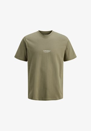 Koszula w kratę z bawełny, noszona na oliwkowej zielonej koszulce, w połączeniu z luźnymi, niebieskimi dżinsami i białymi trampkami.