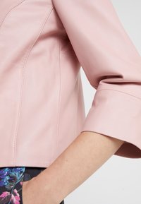 Rosa läderjacka i cropped-stil med en slät yta, med trekvartsärmar och synliga sömdetaljer. Inkluderar en sidoficka.