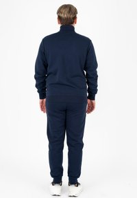 Completo da ginnastica blu navy con colletto alto e polsini a coste, caratterizzato da un design slim fit. Texture morbida, abbinato a scarpe da ginnastica bianche.