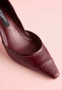 Scarpa in pelle bordeaux con punta affusolata, design a taglio basso, texture liscia e dettagli di cucitura minimi sulla parte superiore.