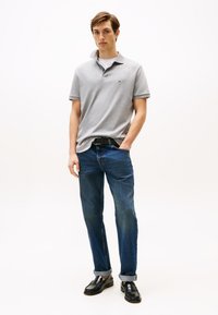 Polo gris avec col, jean denim bleu et mocassins noirs. Coupe slim avec manches retroussées et petit logo sur le polo.