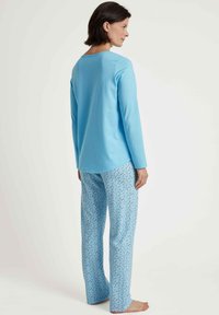 Lichtblauw langslaven topje gecombineerd met gestreepte blauwe pyjamabroek met kleine, meerkleurige bloemenpatronen. Zachte stof, relaxte pasvorm.