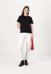 Sort t-skjorte i bomull, korte ermer, rund hals, kombinert med hvite denim jeans. Holder en liten rød håndveske, iført svarte ankelstøvler.