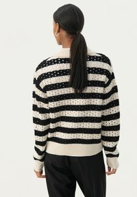 Pull rayé noir et crème avec un tricot texturé, des poignets et un ourlet côtelés, un motif d'ouverture tissé et une coupe décontractée.