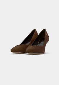 Chaussures à talons hauts en daim marron avec un design à bout pointu, présentant une texture lisse et un petit emblème sur le côté.