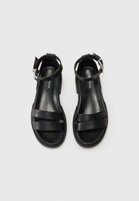 Sorte skinnsandaler med to brede stropper, ankelspenne og teksturert såle. Glatt finish, minimalisk design og flat hæl.
