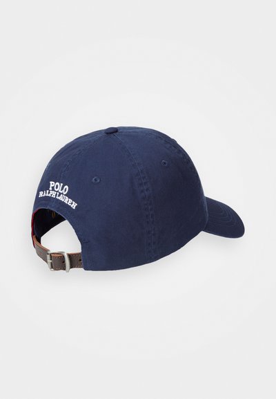 Námornícky modrá bavlnená šiltovka s nastaviteľným hnedým koženým popruhom. Na zadnej strane sa nachádza biele vyšívané logo "Polo Ralph Lauren".