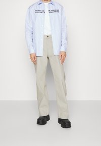 Camisa de botones a rayas azul claro, pantalones de pierna ancha color beige y zapatos gruesos negros. Texto impreso en la camisa. Tela suave y corte relajado.