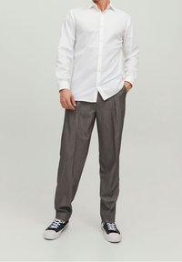 Vit skjorta med knäppning, grå ränderade byxor och svarta sneakers med vita sulor. Skjortan har en spetsig krage och en slät textur.